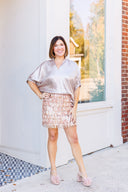 Woman wearing a silver blouse and rose gold sequin skirt standing in front of a white door.