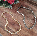 Two necklaces, one gold and one silver, on a wooden surface with a floral background.
