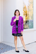 Bright purple sequin blazer jacket and black leather mini skirt with large purple bead necklace.