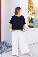 Woman wearing a black top with adjustable drawstring waist with ivory wide-leg pants.