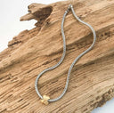 Silver braided necklace with a gold accent on a wooden surface