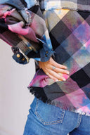 Person wearing a plaid jacket with pink and black patterns, holding a colorful scarf.