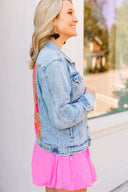 Woman wearing a denim jacket and pink dress with colorful accents outdoors.