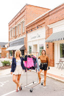 Two women with a rack of clothes in front of a brick building with 'Laundry Dae' sign.