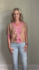 Video of woman in beige knitted sweater with pink bow detail and trim.
